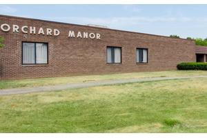 A brick building named 'Manor' with windows and a grassy front yard.