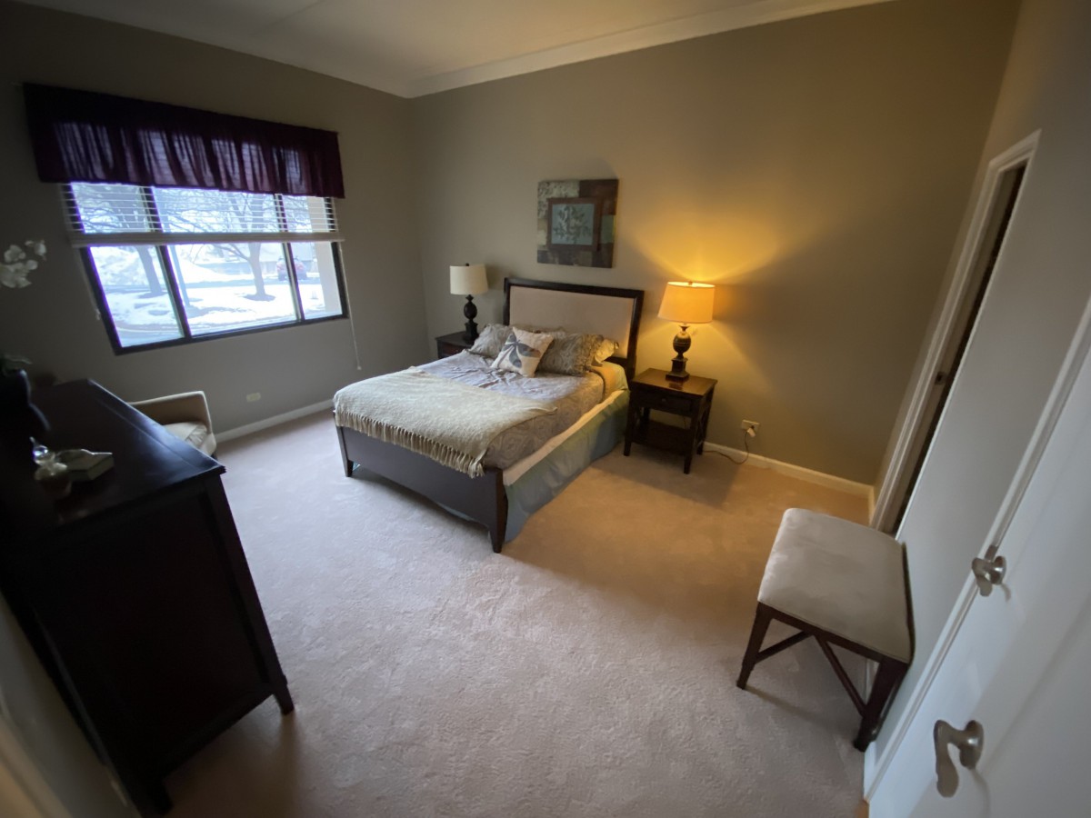 A cozy bedroom featuring a bed with a headboard, a lamp on the nightstand, and a window allowing natural light.