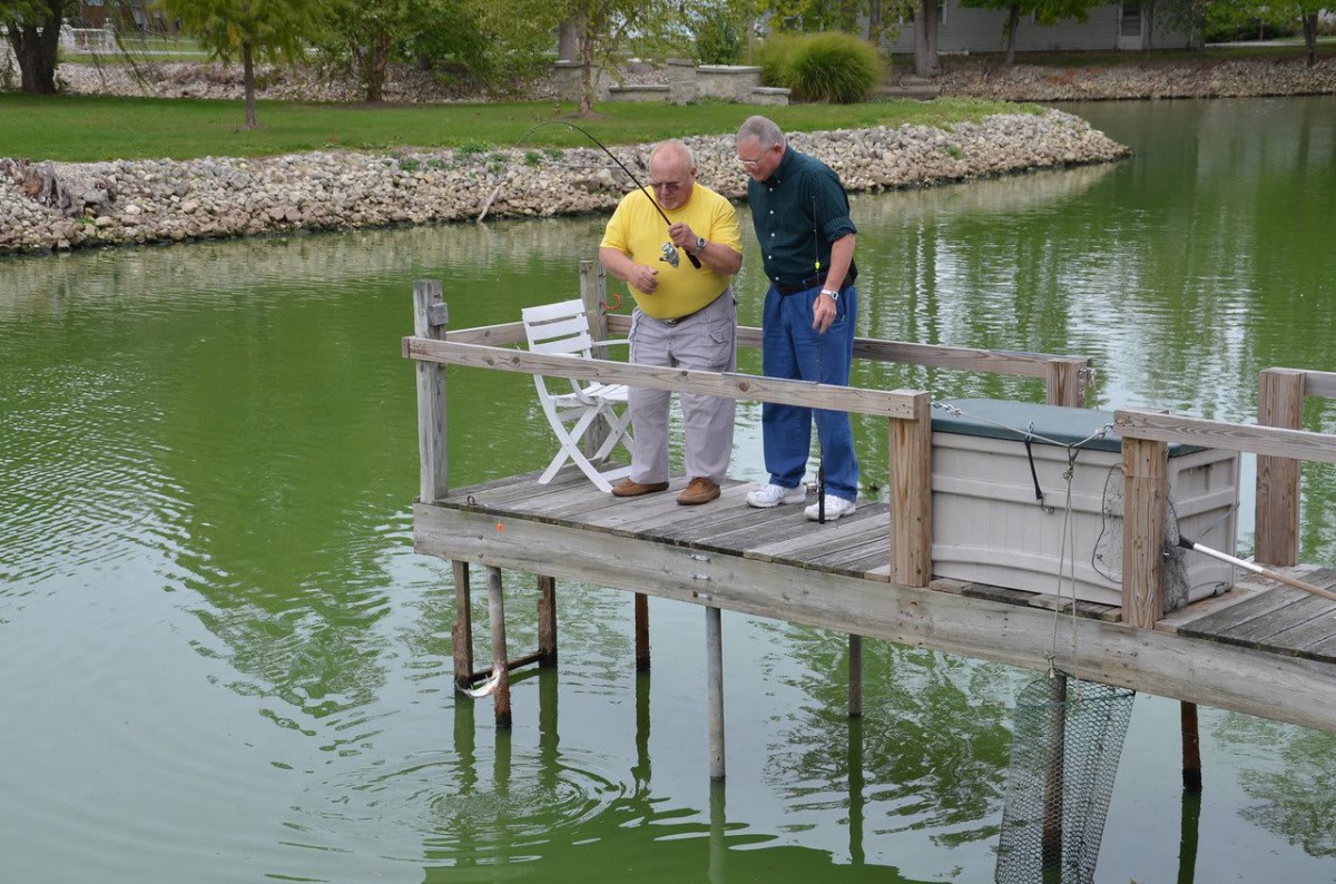 Two people fishing from a dock by a lake.