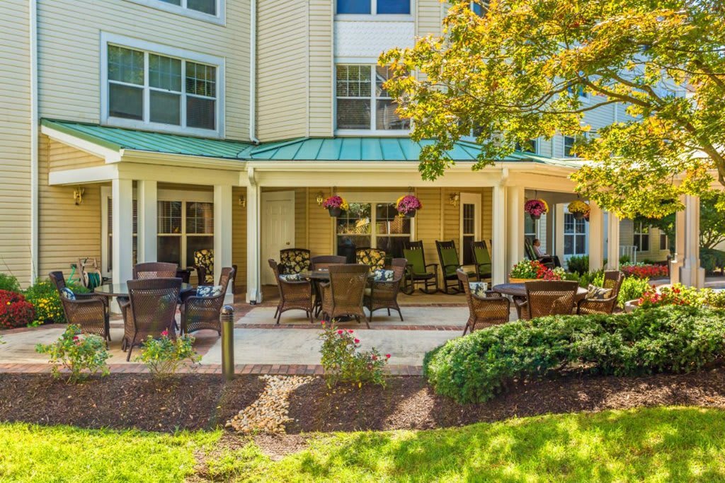 A cozy patio area with outdoor furniture outside a residential building, surrounded by lush greenery.