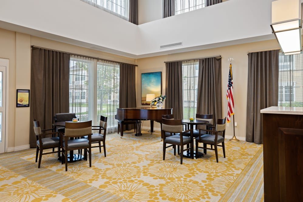 A spacious and well-lit meeting room with arranged tables and chairs, featuring a grand piano and an American flag.