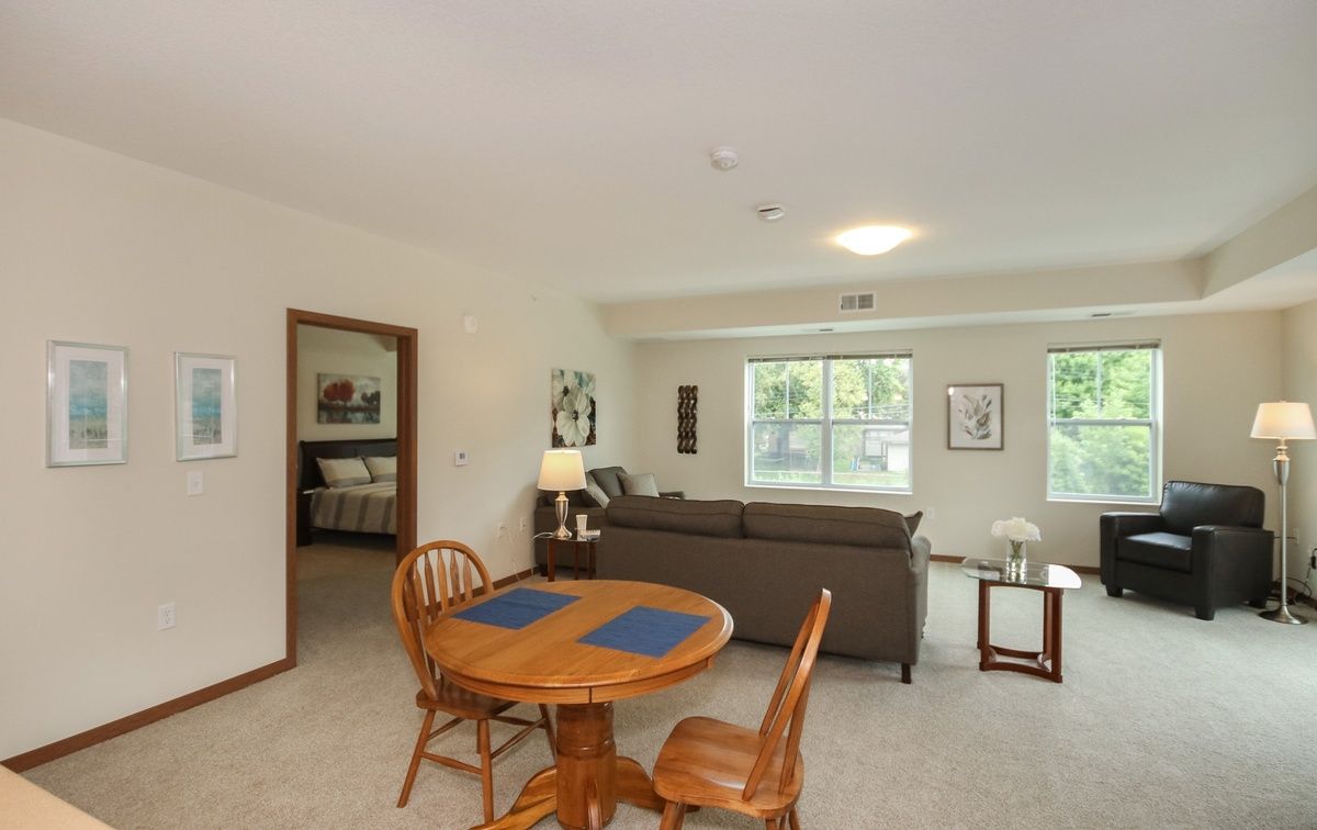 A cozy living space featuring a dining area with a wooden table and chairs, adjacent to a seating area with a sofa and large windows.