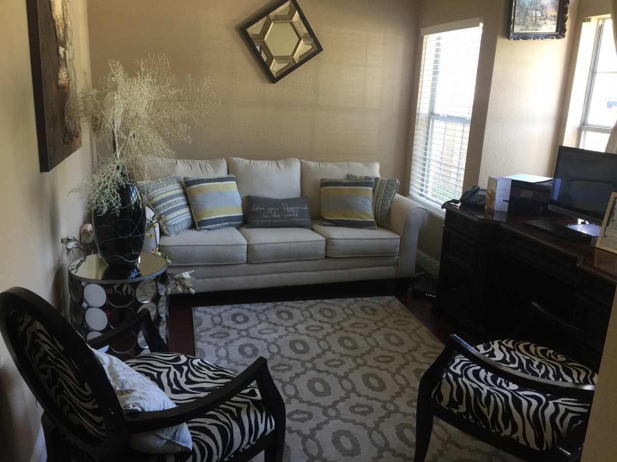 A cozy living room featuring a sofa with cushions, patterned chairs, a decorative rug, and wall art.