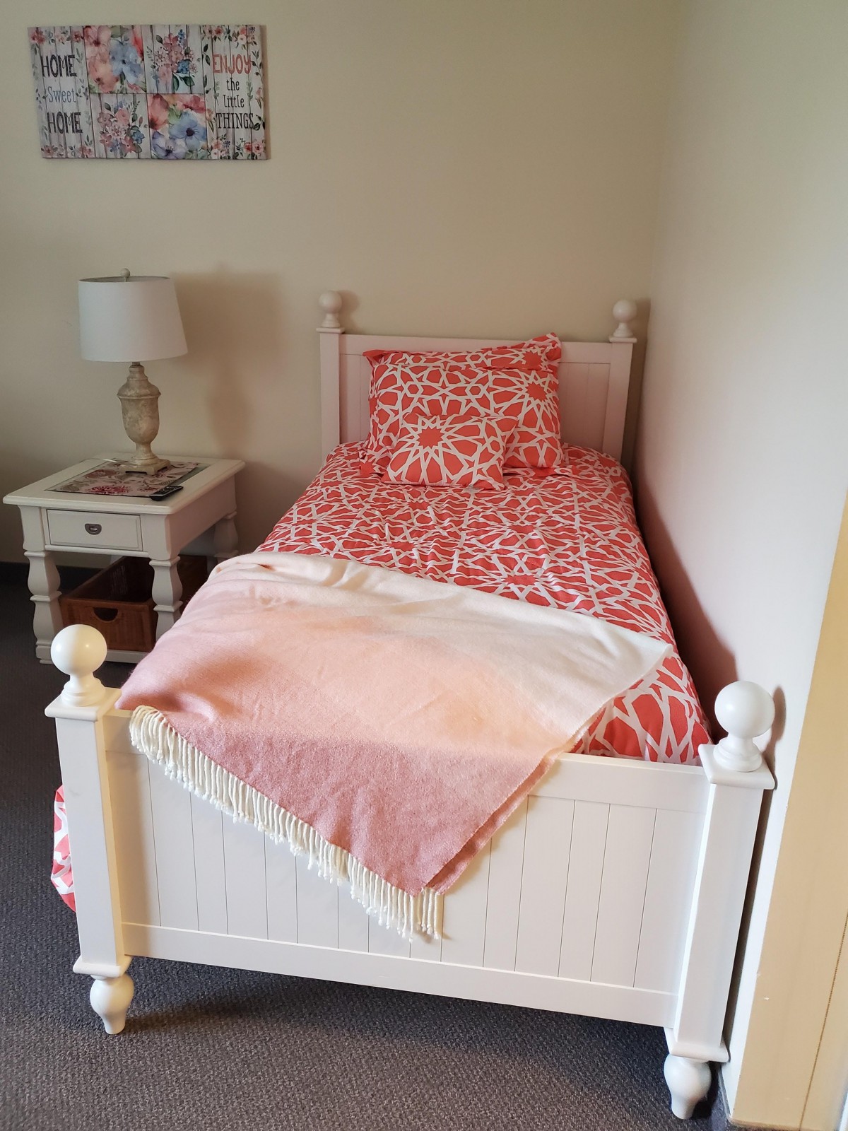 A cozy bedroom corner with a single bed adorned in pink patterned bedding and a bedside table with a lamp.