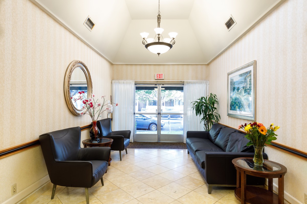 A well-lit lobby with black seating, decorative plants, and a chandelier.