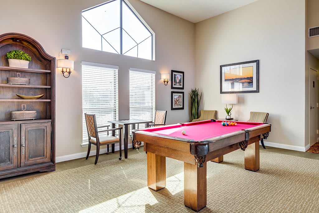 A well-lit recreation room featuring a red pool table and comfortable seating near large windows.