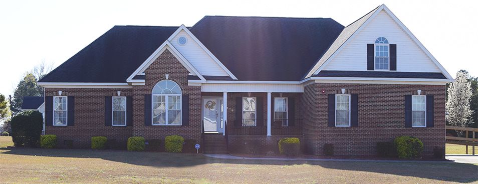 A brick exterior house with a porch and multiple windows.