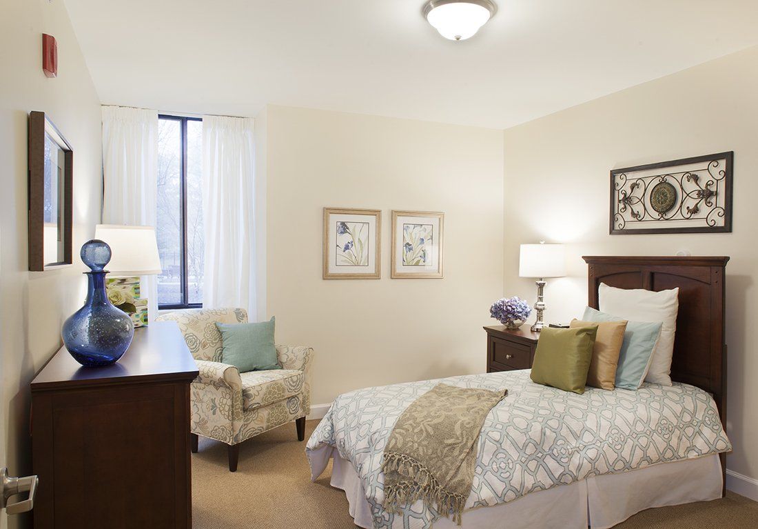 A cozy bedroom with elegant decor, featuring a neatly made bed, artwork on the walls, and a comfortable armchair.