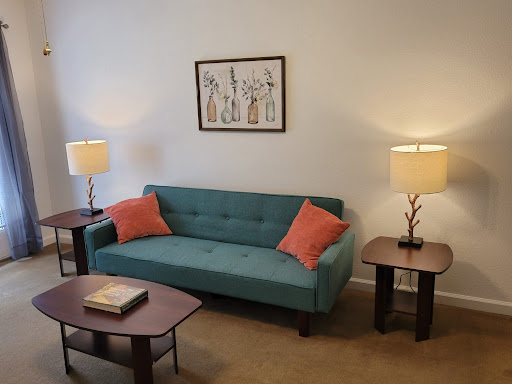 A cozy living room featuring a teal sofa with orange cushions, paired with stylish lamps and elegant artwork.