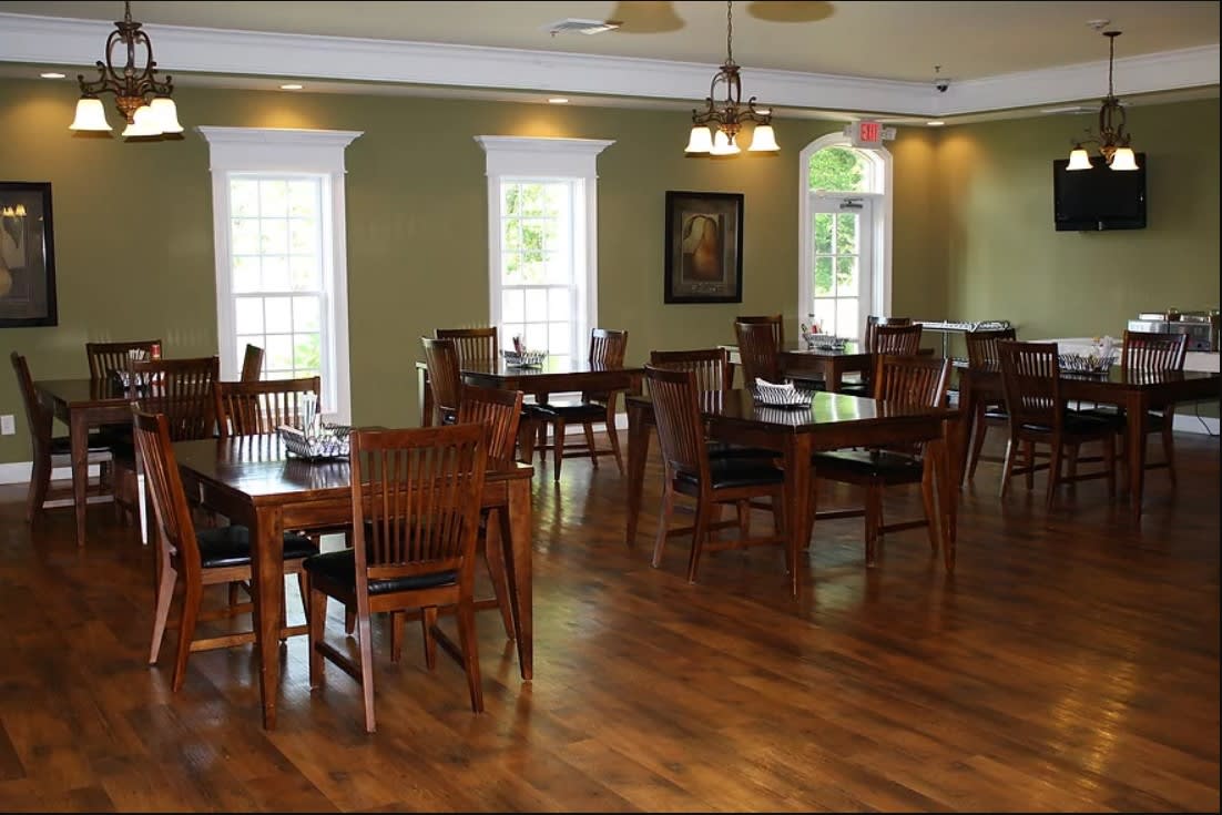 An empty dining room with wooden tables and chairs, featuring large windows and elegant lighting.