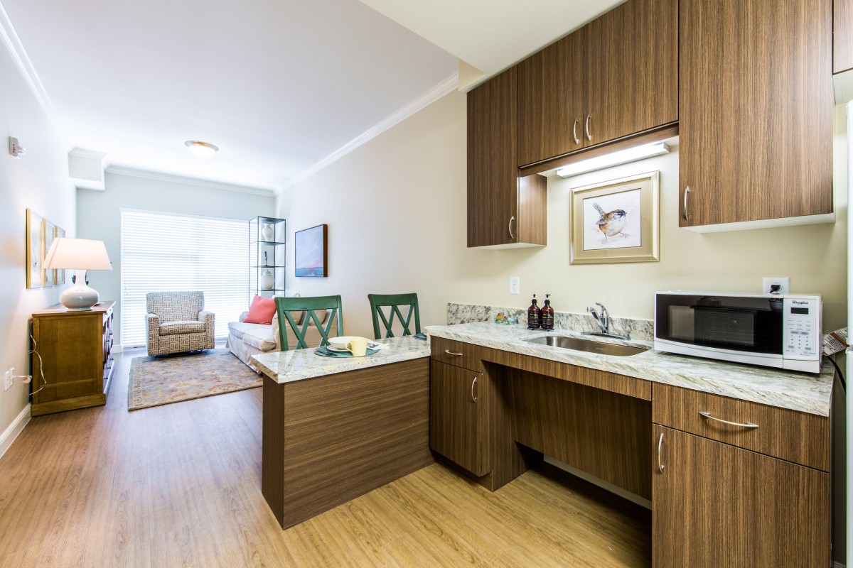 A modern apartment kitchen with wooden cabinets and an adjoining living area.