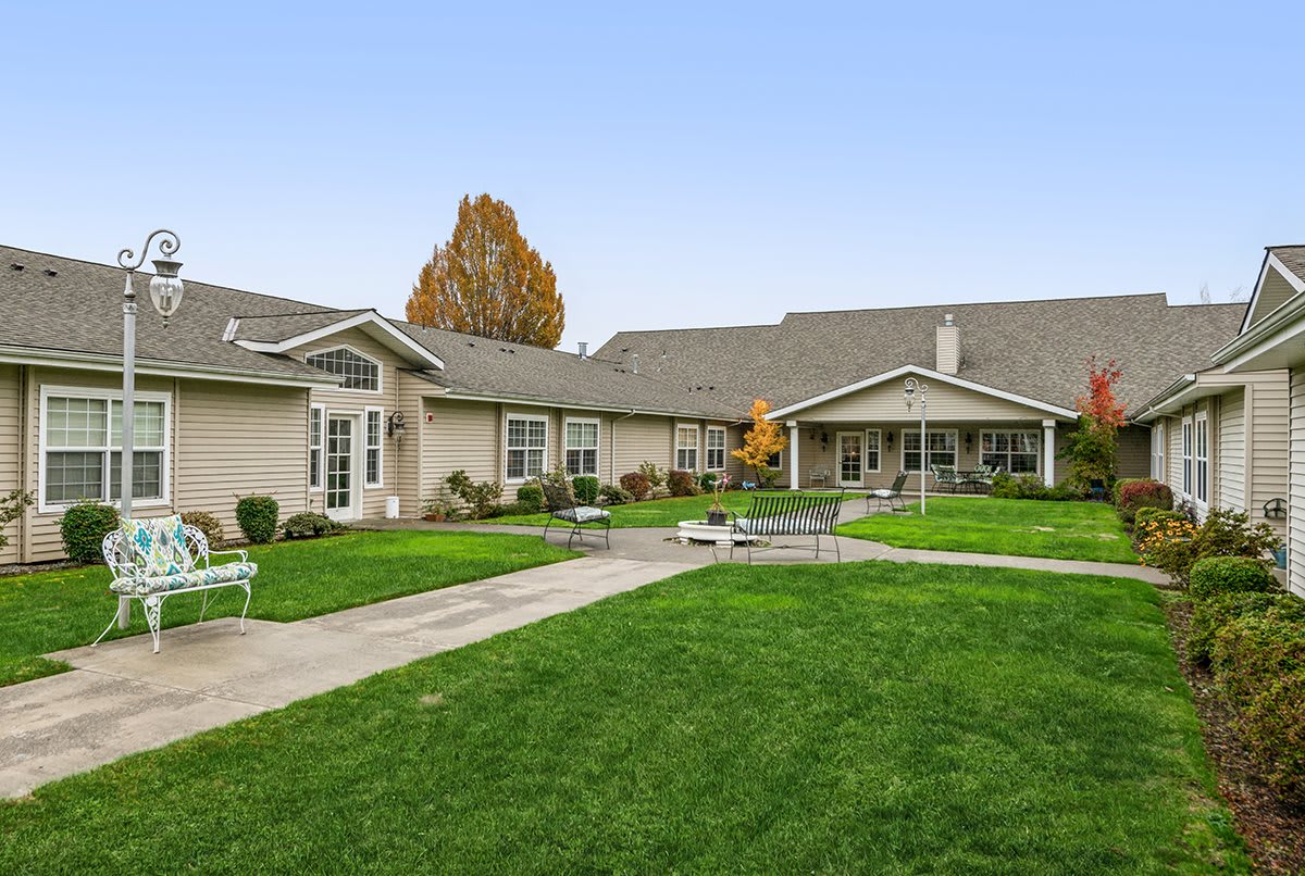A well-maintained residential building with a green lawn and benches, surrounded by autumn trees.
