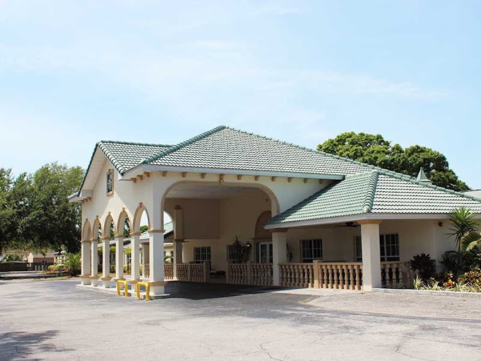 A building with arched columns and a green roof, surrounded by a parking area.