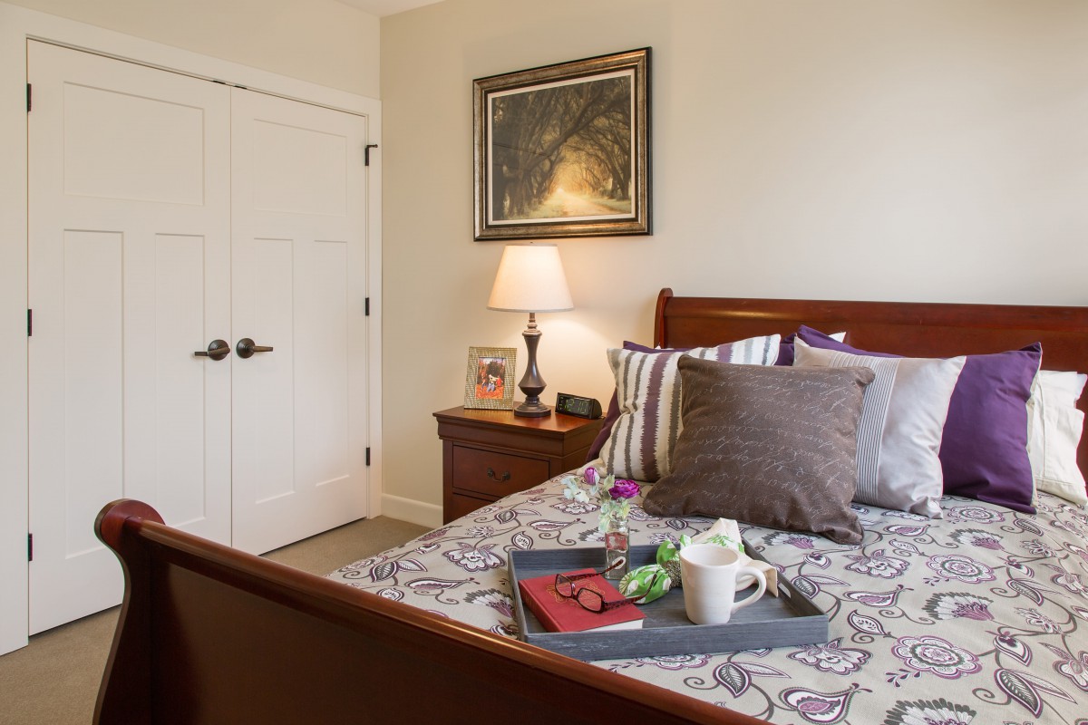 A cozy bedroom with a neatly made bed, featuring decorative pillows, a framed artwork on the wall, and a bedside table with a lamp.