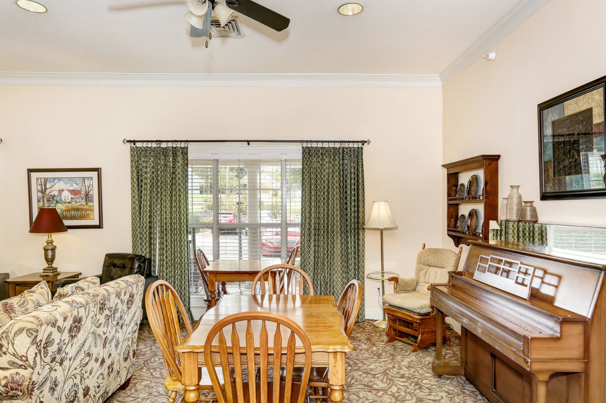 A cozy living room with a dining area, featuring a piano and a set of wooden table and chairs.