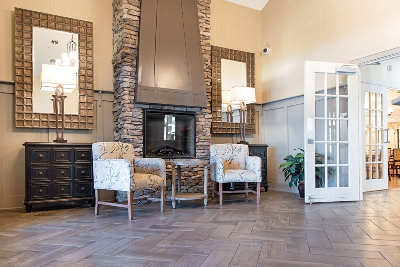 A modern living room with a stone fireplace, stylish chairs, and wooden flooring.