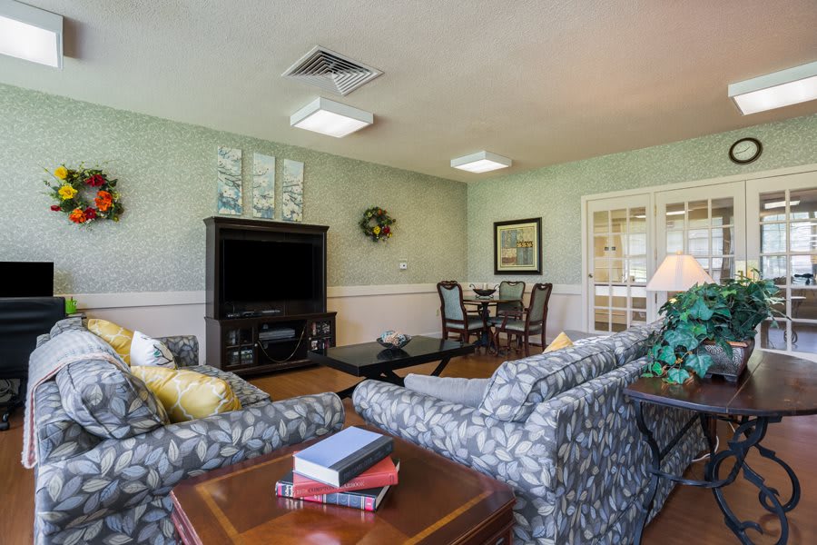 A cozy living room featuring patterned sofas, a television, a coffee table, and decor elements such as paintings and a wreath.
