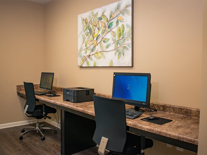 A small office setup with desks featuring computers and a printer, complemented by artwork on the wall.