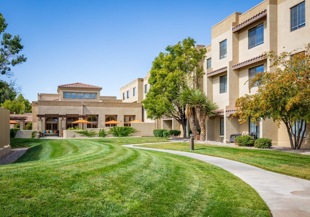 A modern residential building with a well-maintained lawn and pathway on a sunny day.