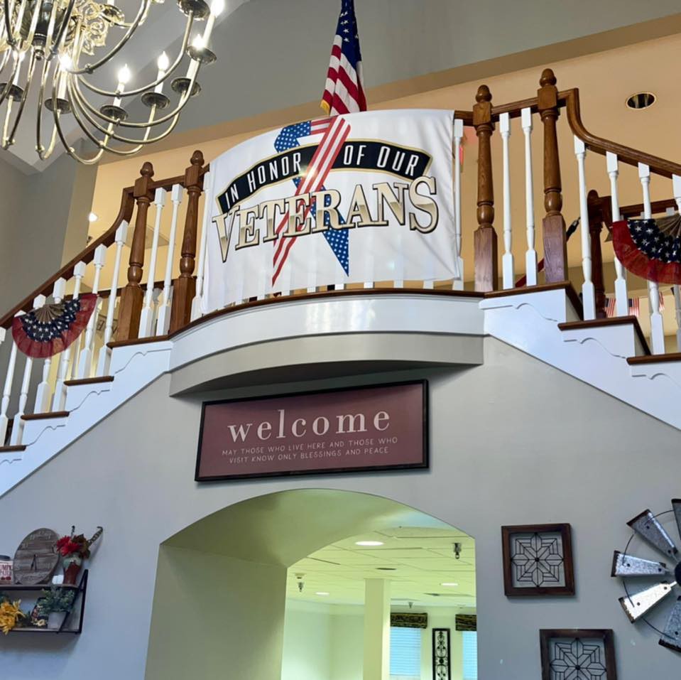 A welcoming interior with a patriotic theme, featuring a banner and elegant chandelier above a staircase.