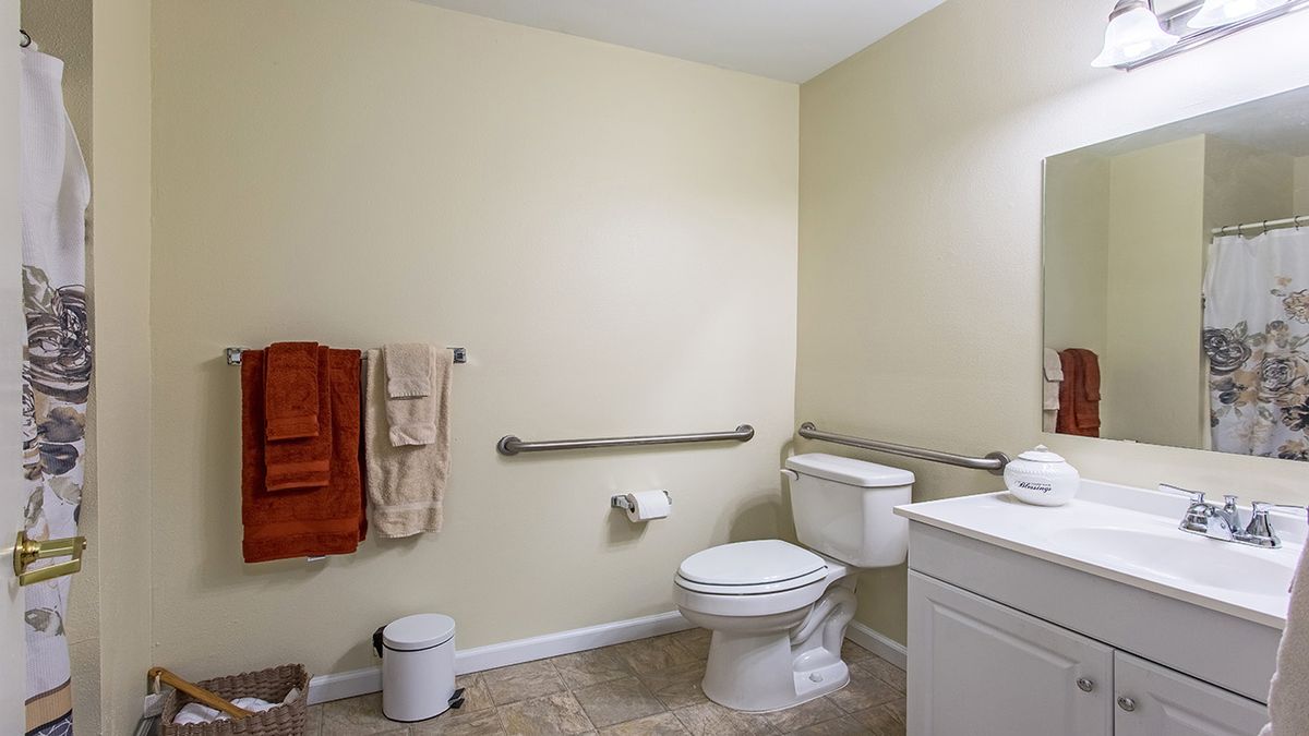 A spacious bathroom with grab bars next to the toilet and sink, featuring a tiled floor and neatly hung towels.
