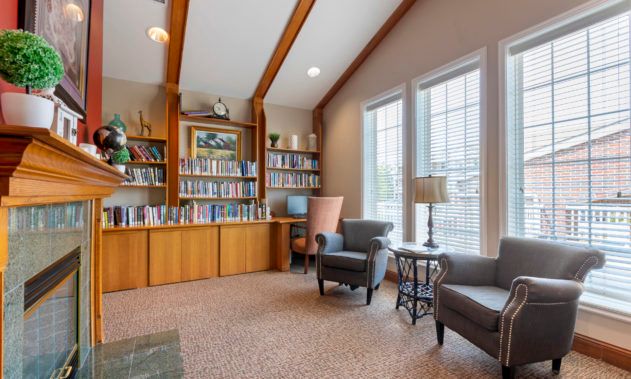 A cozy library nook with bookshelves, armchairs, and a desk in a well-lit room.