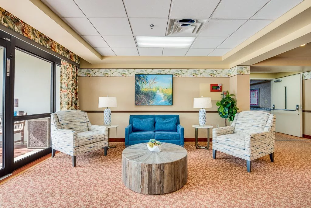 A cozy living room arrangement with a blue sofa, two patterned chairs, a round wooden table, and warm lighting.