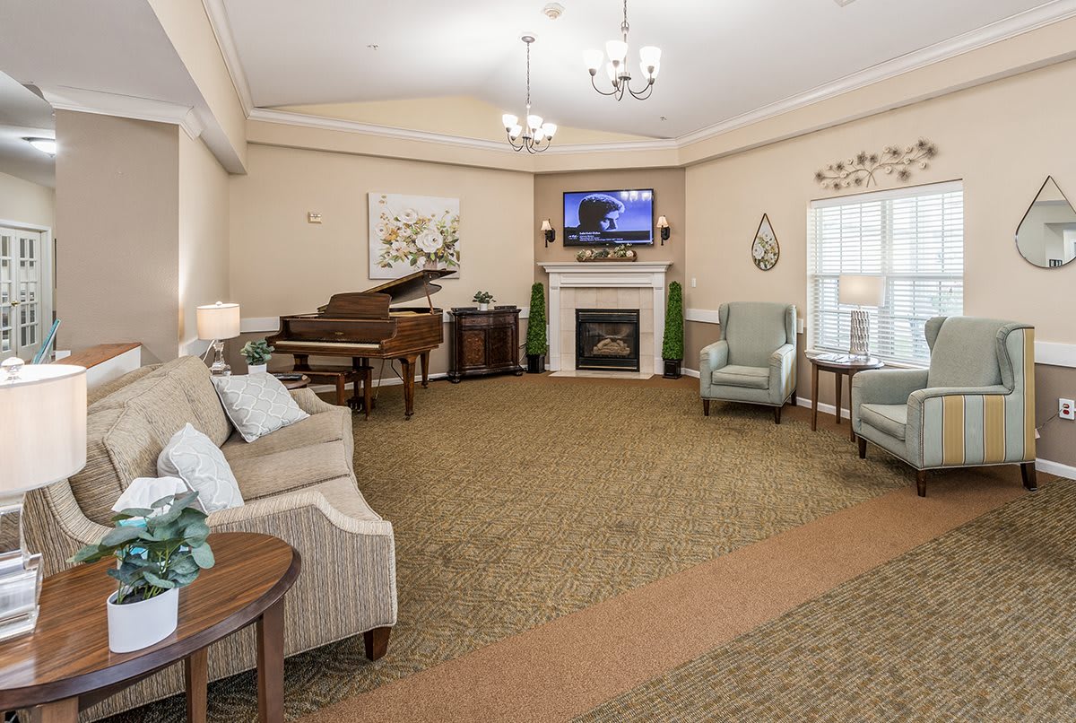 A cozy living room with a grand piano and a fireplace, featuring elegant decor and comfortable seating.
