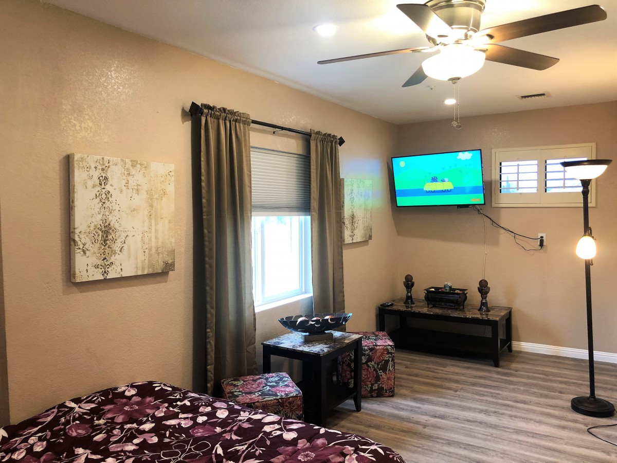 Cozy bedroom featuring a ceiling fan, wall-mounted television, and stylish decor.
