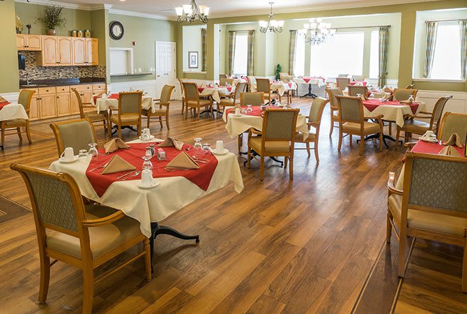 An elegant dining room with neatly arranged tables and chairs, featuring wood flooring and chandeliers.