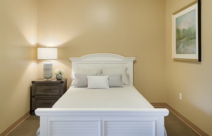 A cozy bedroom with a white bed and a nightstand with a lamp.