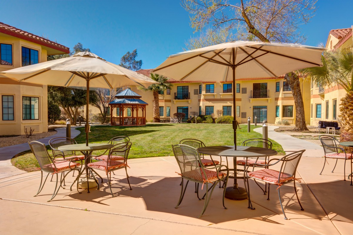 A sunny outdoor patio with tables and umbrellas overlooking a landscaped garden.