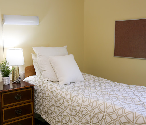 A cozy bedroom featuring a neatly made single bed with decorative pillows, alongside a nightstand and lamp.