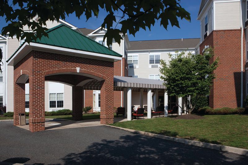 A residential building with a covered entrance and surrounding greenery on a sunny day.