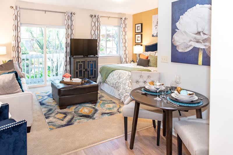 A cozy studio apartment with a combined living and sleeping area, featuring modern decor and a small dining table.