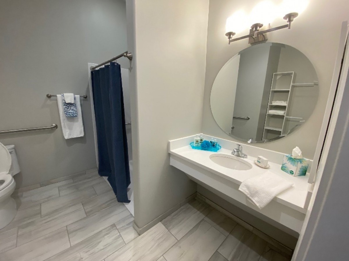 A modern bathroom with a large vanity mirror, tiled flooring, and a shower area with a blue curtain.