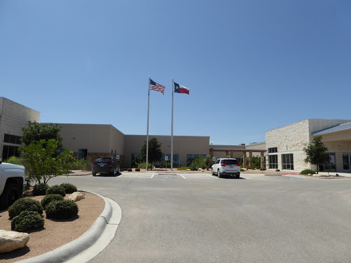 A view of a building with American and state flags flying in front, set against a clear blue sky.
