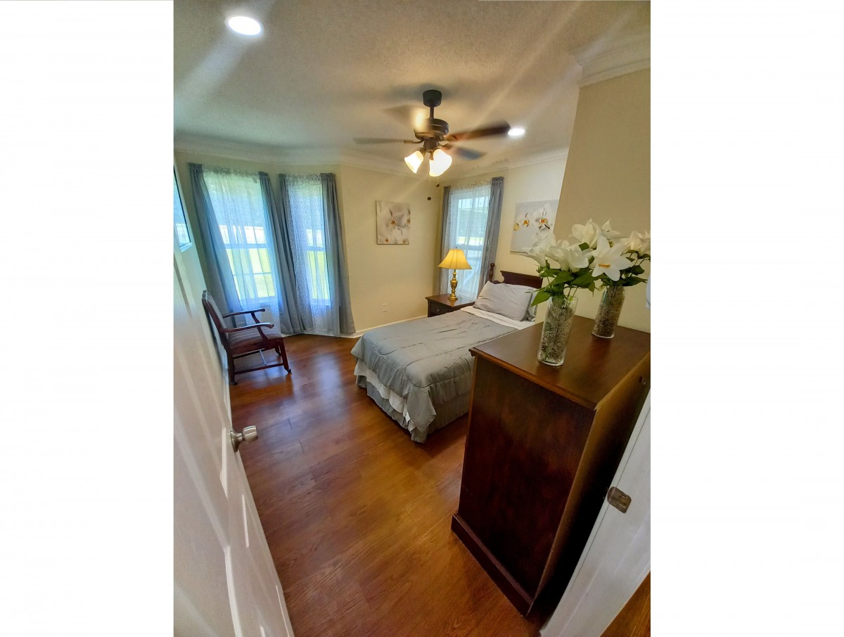 A cozy bedroom with a bed, dresser, ceiling fan, and hardwood flooring.