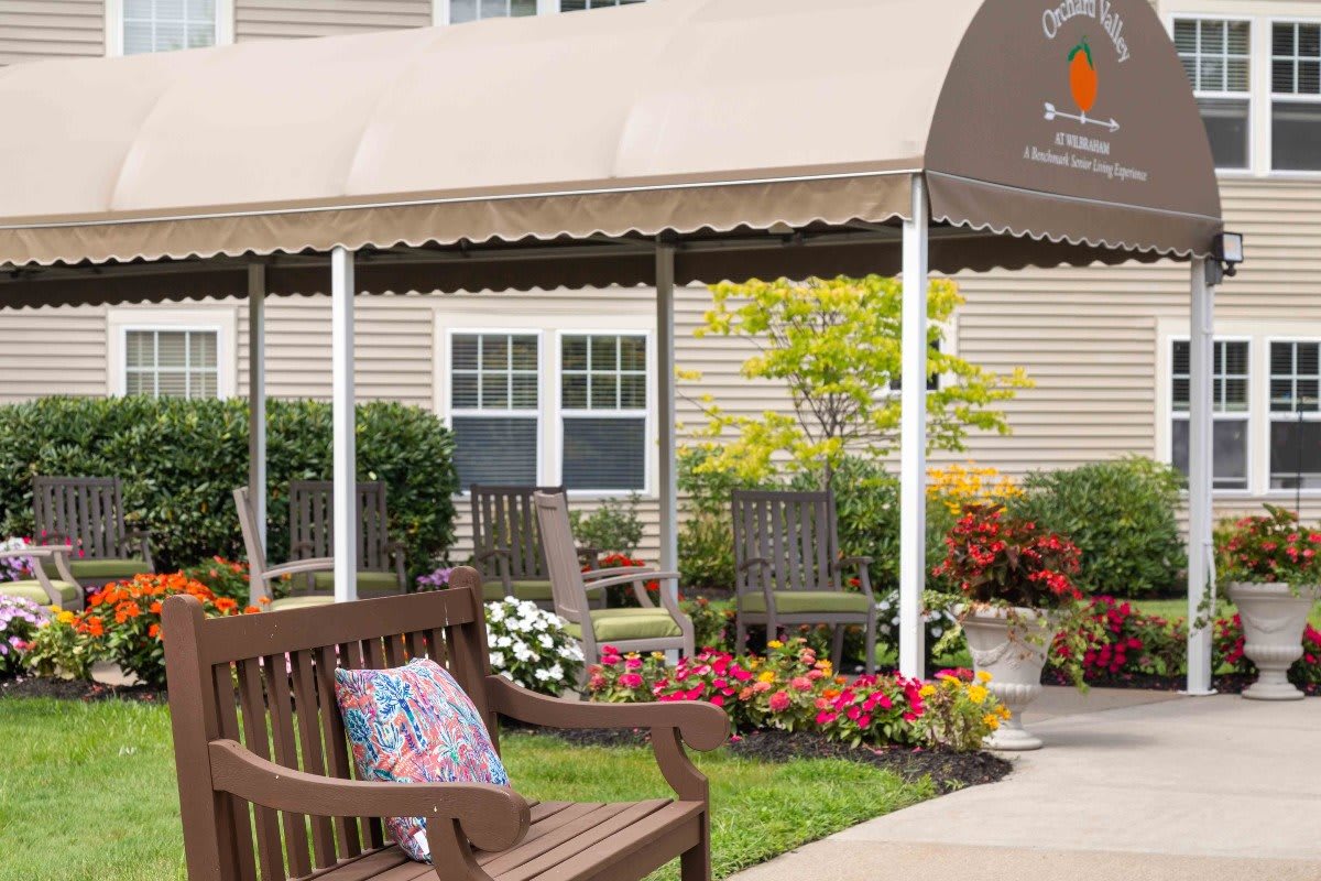 A cozy outdoor seating area featuring benches, colorful flowers, and a shaded awning.
