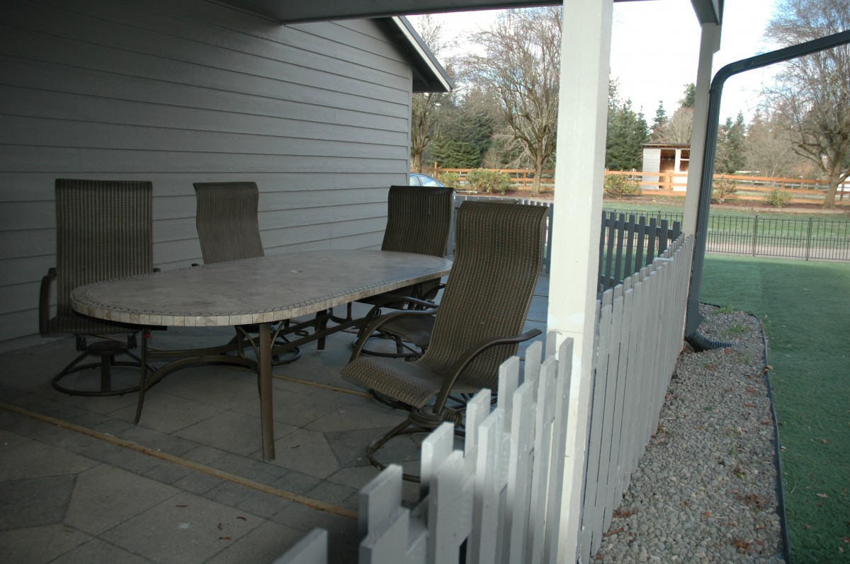 A covered patio with a table and chairs next to a backyard fence.