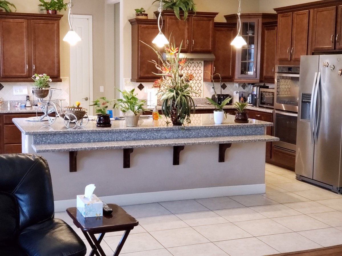 A modern kitchen with wooden cabinets, a large countertop adorned with plants, and stylish pendant lighting.