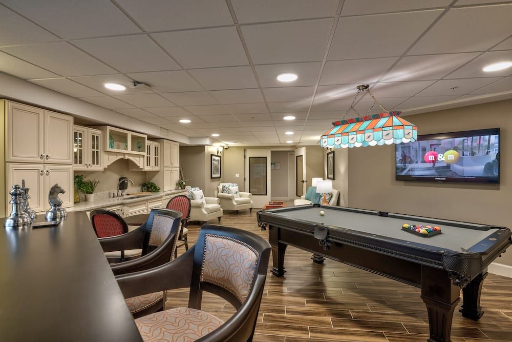 A modern basement game room featuring a pool table, bar seating, and a television.