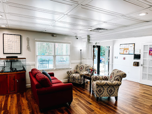 A cozy living room featuring a red couch and patterned chairs, illuminated by natural light.