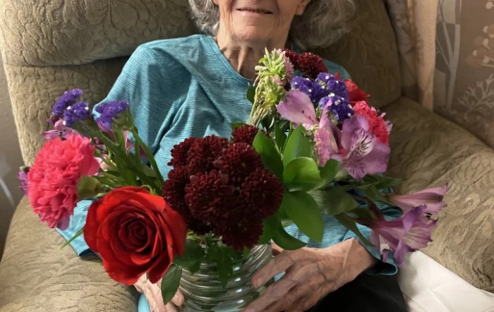 An elderly woman sitting and holding a colorful bouquet of flowers.