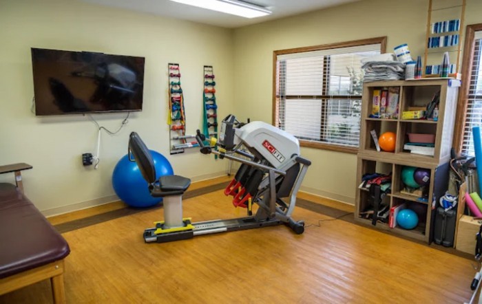 A therapy room equipped with a recumbent bike, exercise ball, and various fitness accessories.