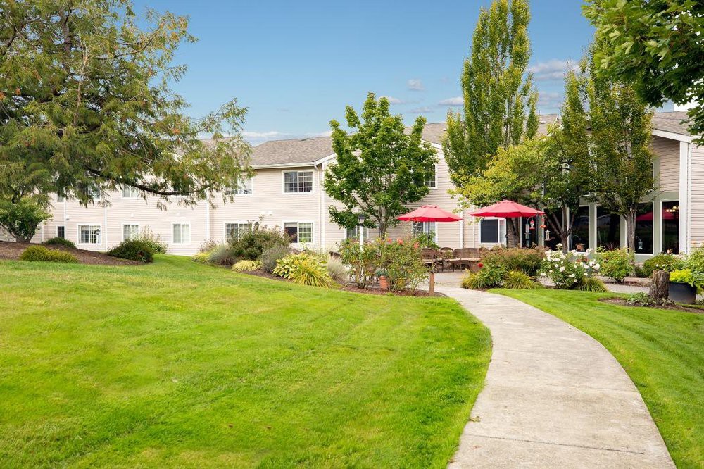 A scenic outdoor garden with a pathway leading to a building, featuring a well-maintained lawn and red patio umbrellas.