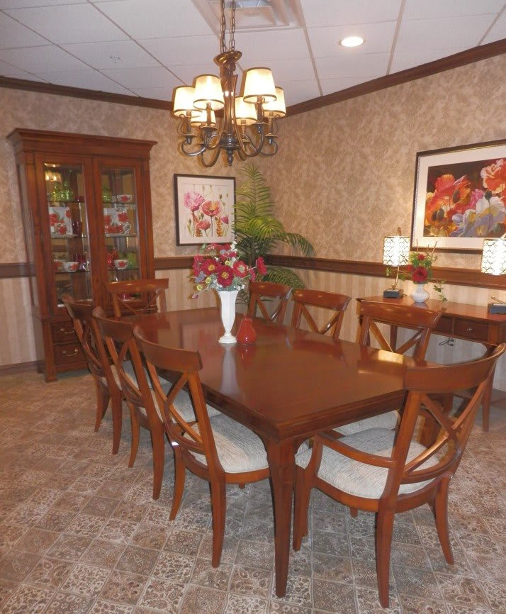 A dining room with a large wooden table surrounded by chairs, a chandelier above, and artwork on the walls.