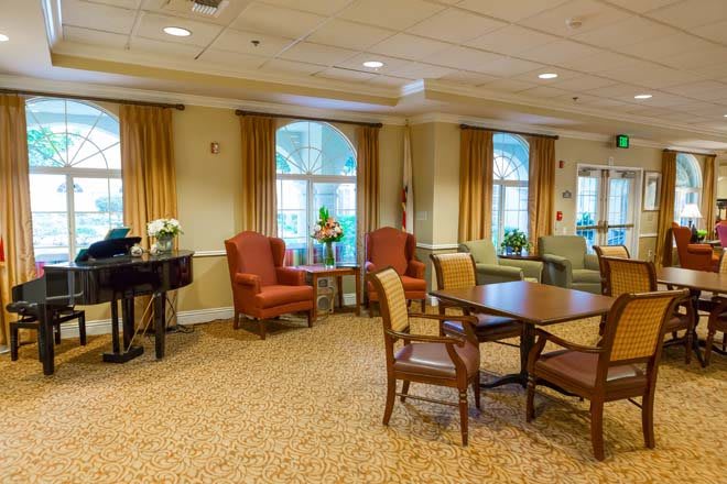 A comfortable seating area with tables and chairs in a carpeted room featuring large windows and curtains.