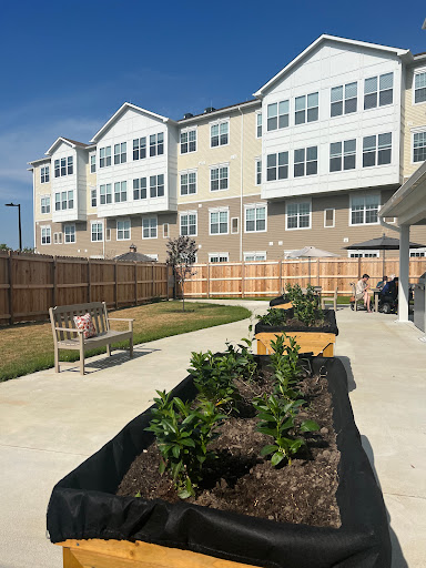 A peaceful garden area featuring raised vegetable beds, surrounded by modern residential buildings.