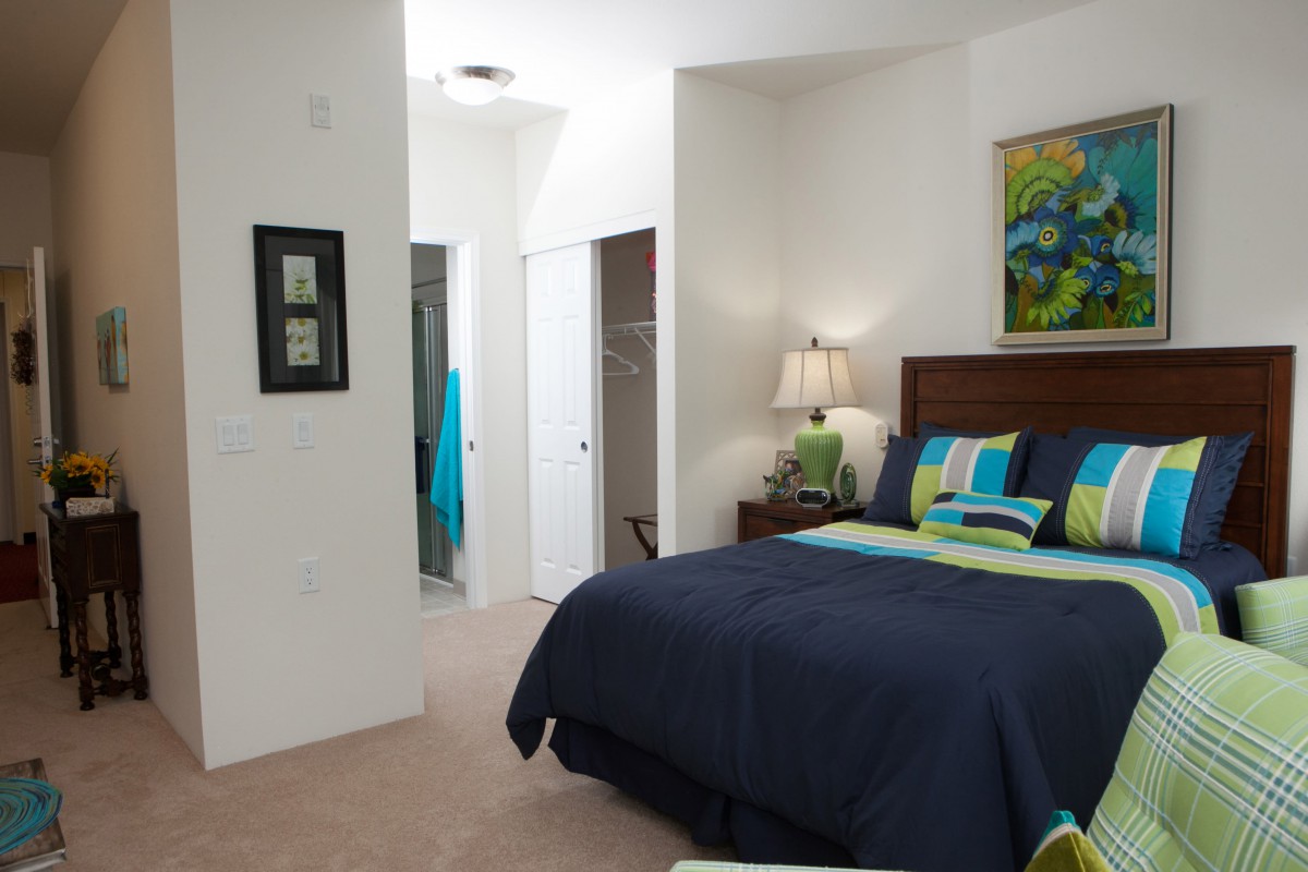 A cozy bedroom featuring a neatly made bed with colorful pillows, a bedside lamp, and decorative artwork on the wall.